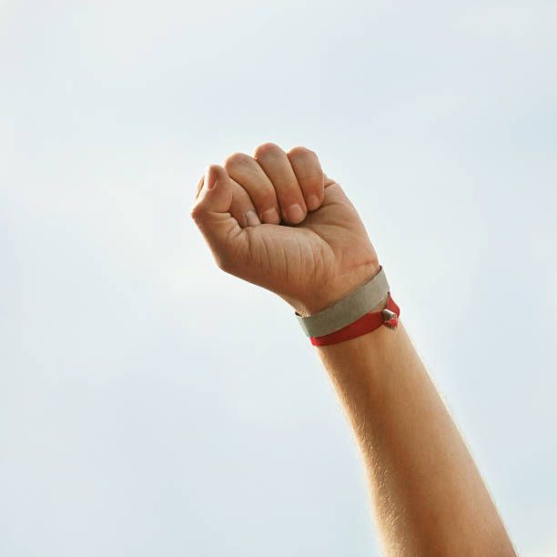 Human hand with red and grey wristband raised against sky